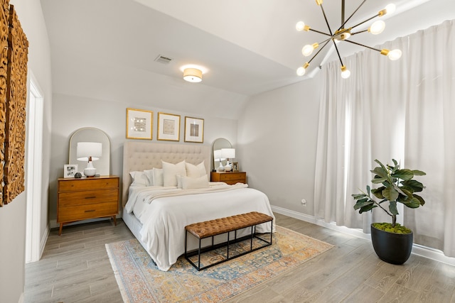 bedroom with lofted ceiling, light hardwood / wood-style floors, and an inviting chandelier