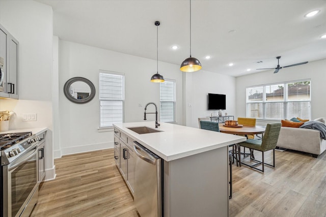 kitchen featuring sink, light hardwood / wood-style flooring, appliances with stainless steel finishes, pendant lighting, and a kitchen island with sink