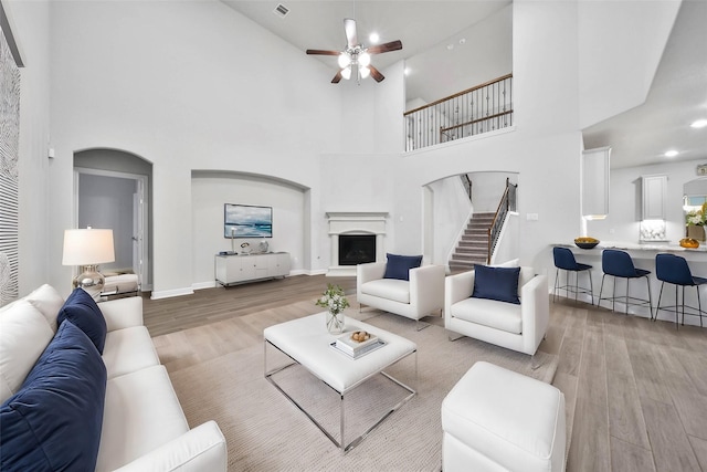 living room featuring ceiling fan, a towering ceiling, and light wood-type flooring