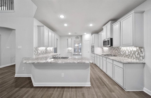 kitchen with white cabinetry, tasteful backsplash, light stone counters, appliances with stainless steel finishes, and kitchen peninsula