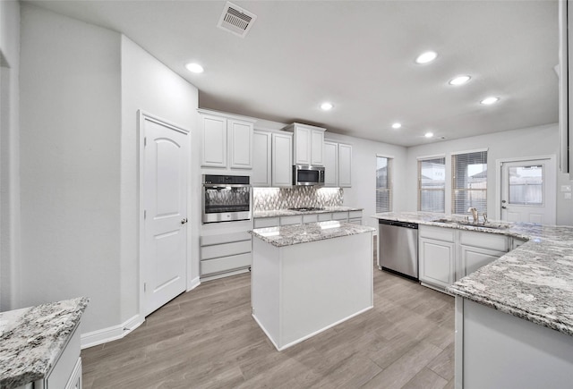 kitchen featuring stainless steel appliances, white cabinetry, a center island, and light stone counters