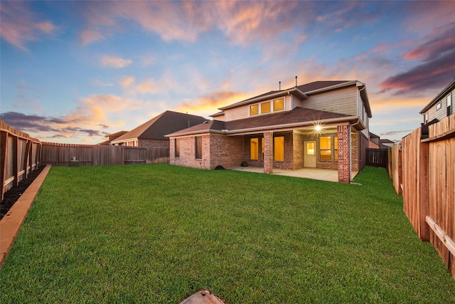 back of property at dusk with a yard, a patio, brick siding, and a fenced backyard