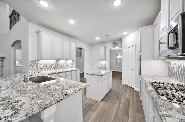 kitchen featuring appliances with stainless steel finishes, backsplash, white cabinets, a center island, and light stone counters