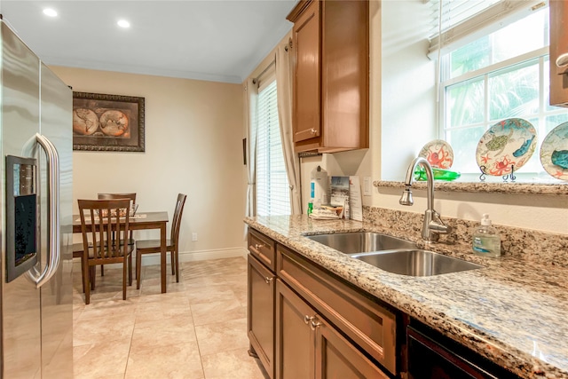 kitchen with stainless steel fridge with ice dispenser, light tile patterned floors, light stone countertops, and sink