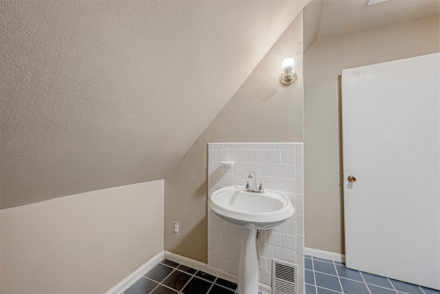 bathroom with tile patterned floors, sink, vaulted ceiling, and a textured ceiling