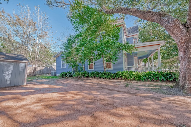 view of side of property with covered porch, a storage shed, fence, and an outbuilding