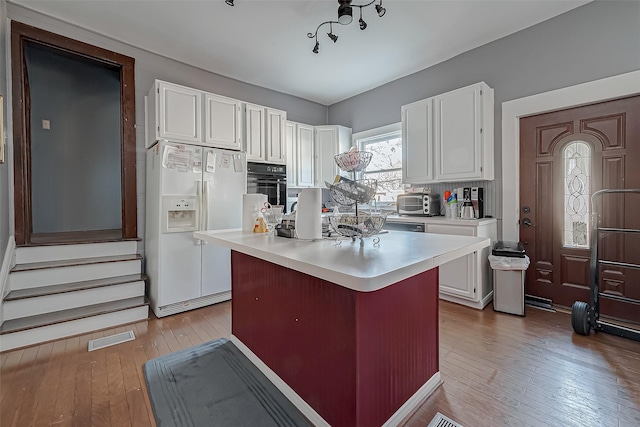 kitchen with light countertops, white refrigerator with ice dispenser, visible vents, and white cabinets