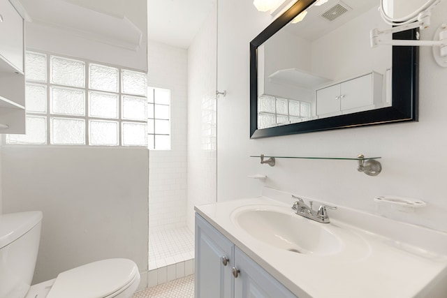 bathroom featuring tile patterned flooring, vanity, a tile shower, and toilet