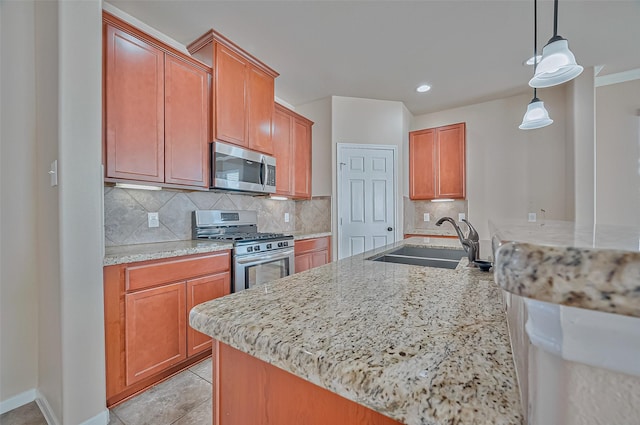 kitchen with sink, backsplash, stainless steel appliances, light stone counters, and decorative light fixtures