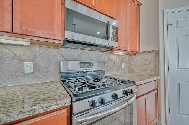 kitchen with light stone countertops, appliances with stainless steel finishes, and backsplash