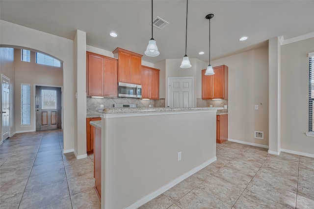 kitchen with light stone counters, a center island, light tile patterned floors, pendant lighting, and backsplash