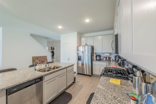 kitchen featuring appliances with stainless steel finishes, sink, light stone counters, and light hardwood / wood-style floors