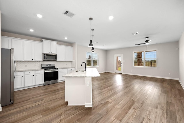 kitchen with an island with sink, sink, white cabinets, hanging light fixtures, and stainless steel appliances