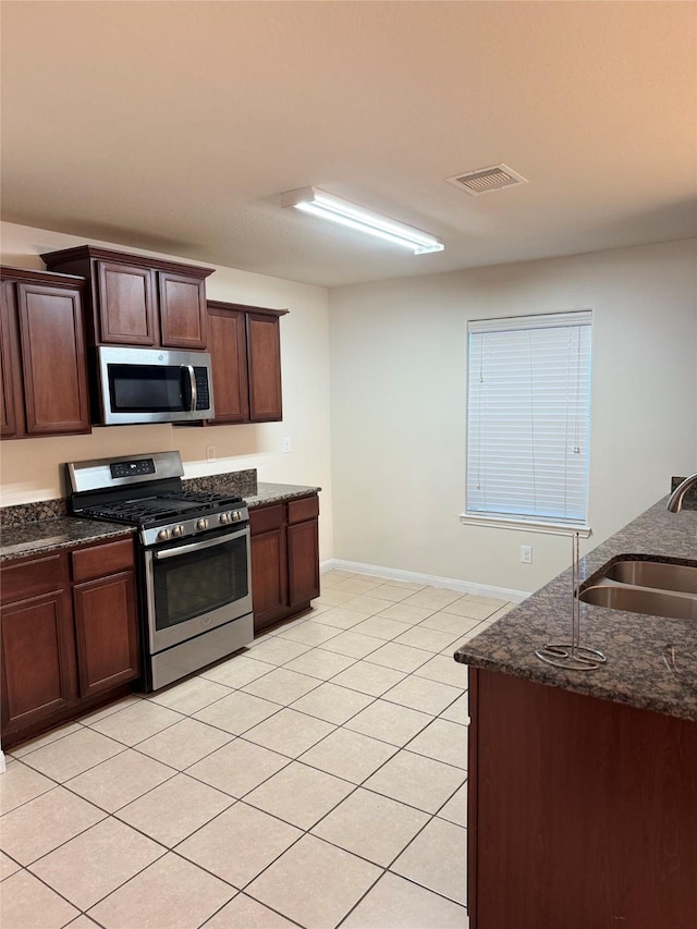 kitchen featuring stainless steel appliances, sink, dark stone counters, and light tile patterned floors