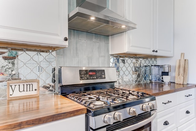 kitchen with wall chimney range hood, butcher block counters, backsplash, white cabinets, and gas range