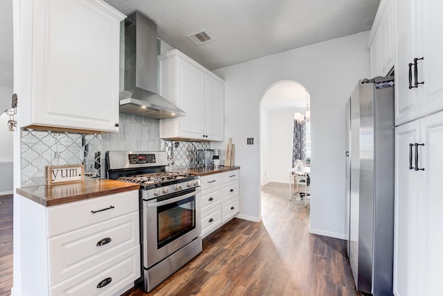 kitchen featuring dark wood-type flooring, butcher block counters, stainless steel appliances, white cabinets, and wall chimney exhaust hood