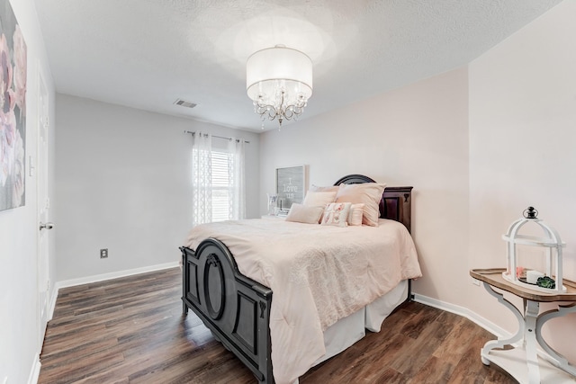 bedroom with dark hardwood / wood-style flooring, a textured ceiling, and an inviting chandelier