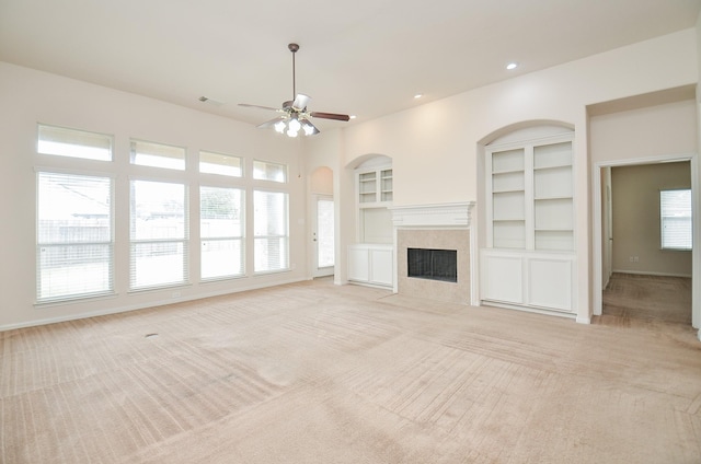 unfurnished living room featuring ceiling fan, a tiled fireplace, light carpet, and built in features