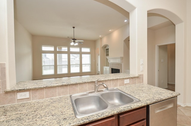 kitchen with a tile fireplace, sink, backsplash, stainless steel dishwasher, and ceiling fan