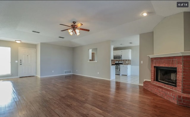 unfurnished living room featuring ceiling fan, a brick fireplace, and light wood-type flooring