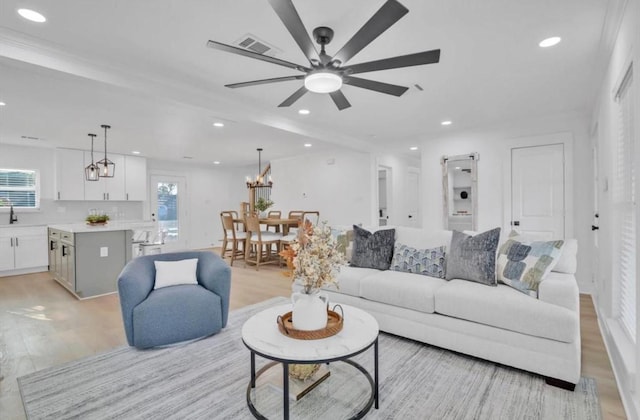 living room featuring sink, beam ceiling, ceiling fan with notable chandelier, and light wood-type flooring