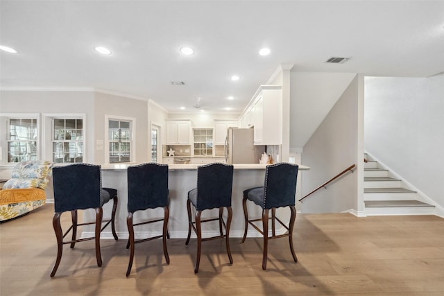 kitchen with white cabinets, stainless steel fridge, a kitchen breakfast bar, kitchen peninsula, and light hardwood / wood-style flooring