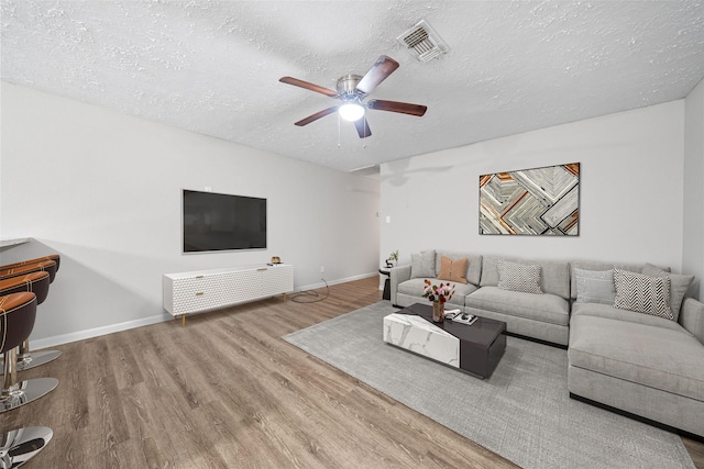 living room with hardwood / wood-style flooring, ceiling fan, and a textured ceiling