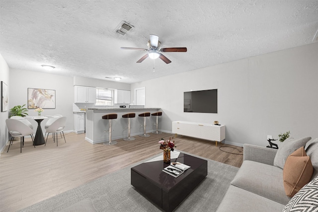 living room featuring ceiling fan, a textured ceiling, and light wood-type flooring