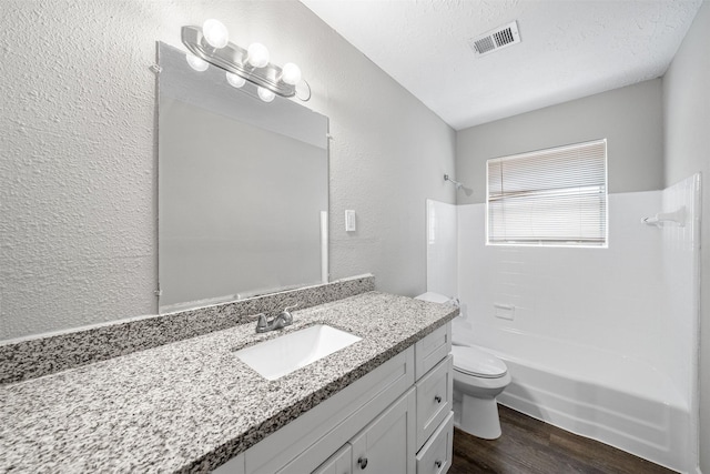 full bathroom featuring hardwood / wood-style flooring, vanity, shower / bath combination, toilet, and a textured ceiling