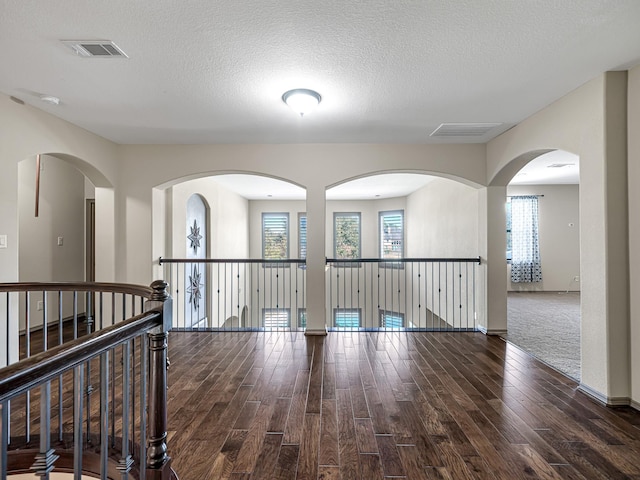 hall featuring a healthy amount of sunlight, dark wood-type flooring, and a textured ceiling