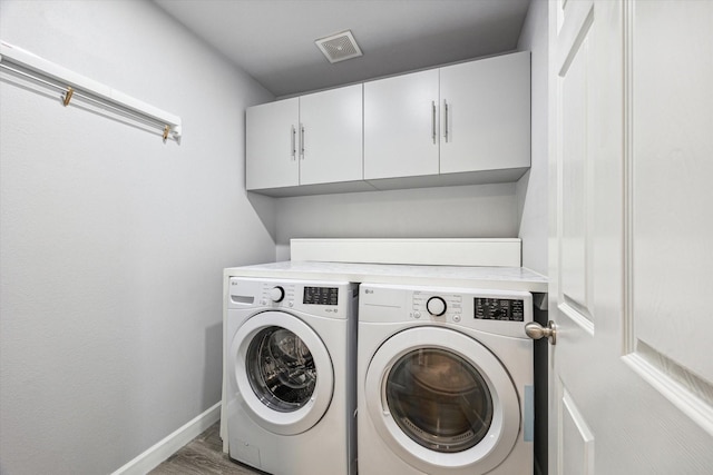 washroom featuring washer and dryer, wood-type flooring, and cabinets