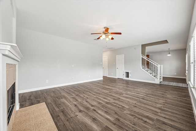 unfurnished living room with dark wood-type flooring, a tile fireplace, and ceiling fan