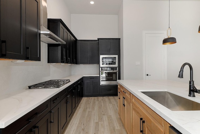 kitchen with sink, wall chimney exhaust hood, stainless steel appliances, light stone countertops, and light hardwood / wood-style flooring