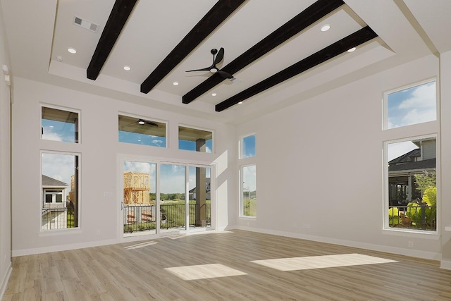 unfurnished living room with beam ceiling, a towering ceiling, light hardwood / wood-style floors, and ceiling fan