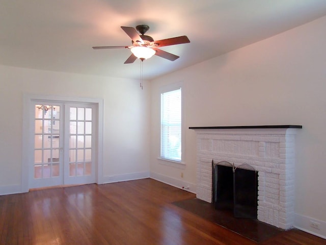 unfurnished living room featuring ceiling fan, a brick fireplace, dark hardwood / wood-style flooring, and french doors