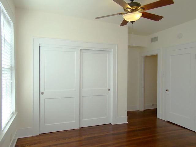 unfurnished bedroom with multiple windows, dark wood-type flooring, ceiling fan, and a closet