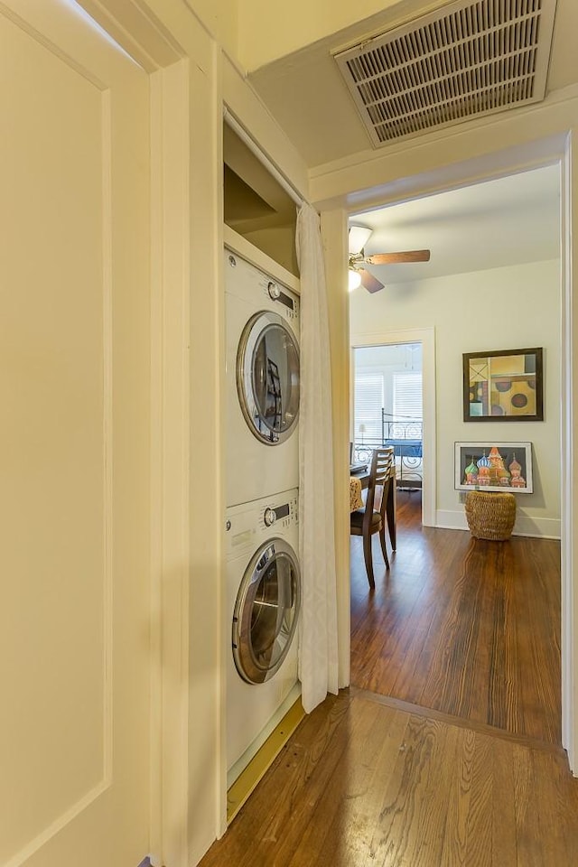 clothes washing area featuring dark wood-type flooring, ceiling fan, and stacked washing maching and dryer