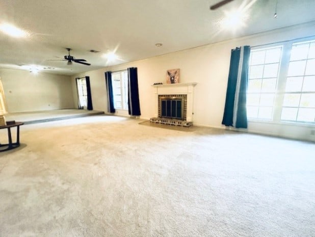 unfurnished living room with ceiling fan, a brick fireplace, carpet flooring, and a wealth of natural light