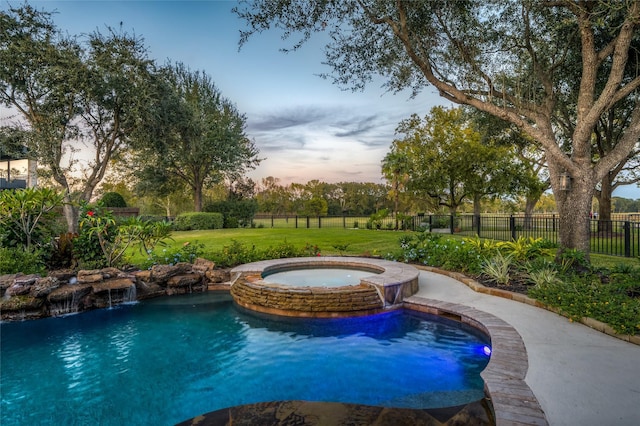 pool at dusk with an in ground hot tub, pool water feature, and a yard