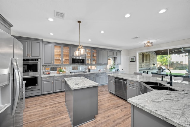 kitchen featuring gray cabinetry, hanging light fixtures, stainless steel appliances, light stone counters, and a kitchen island