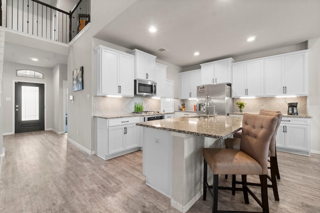 kitchen with a center island with sink, light wood-type flooring, appliances with stainless steel finishes, light stone countertops, and white cabinets