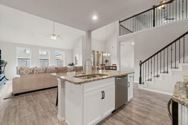 kitchen with an island with sink, sink, white cabinets, stainless steel dishwasher, and light stone counters