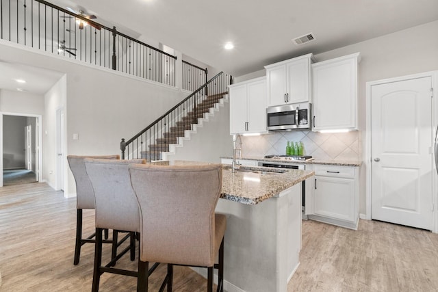 kitchen with a breakfast bar, white cabinets, light stone countertops, a center island with sink, and light wood-type flooring