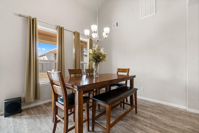 dining area with hardwood / wood-style flooring, a towering ceiling, and a chandelier