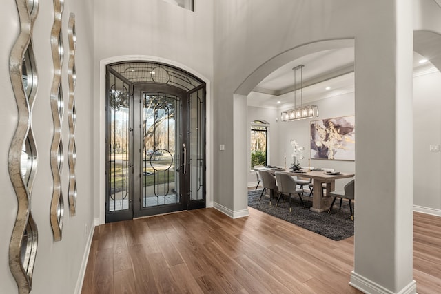 entrance foyer with hardwood / wood-style flooring, a raised ceiling, a towering ceiling, and crown molding