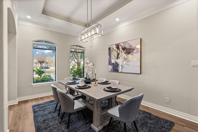 dining room with a tray ceiling, ornamental molding, and light wood-type flooring