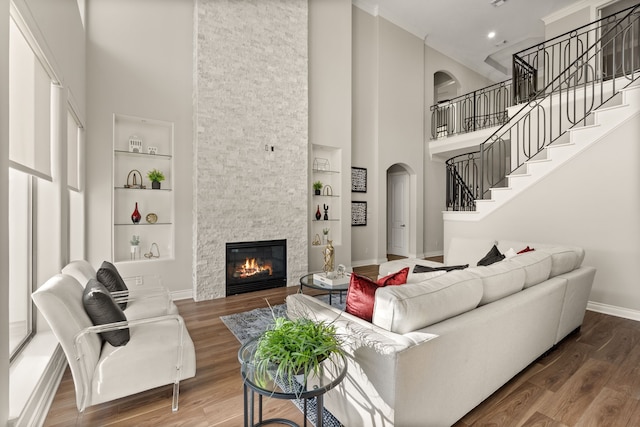 living room with wood-type flooring, a towering ceiling, a fireplace, and built in shelves