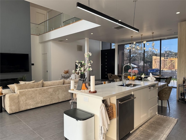 kitchen with sink, an island with sink, pendant lighting, a wall of windows, and white cabinets