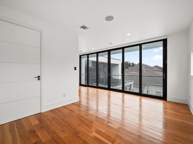 empty room with expansive windows, light wood-style flooring, visible vents, and baseboards