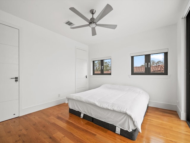 bedroom featuring a ceiling fan, visible vents, baseboards, and wood finished floors